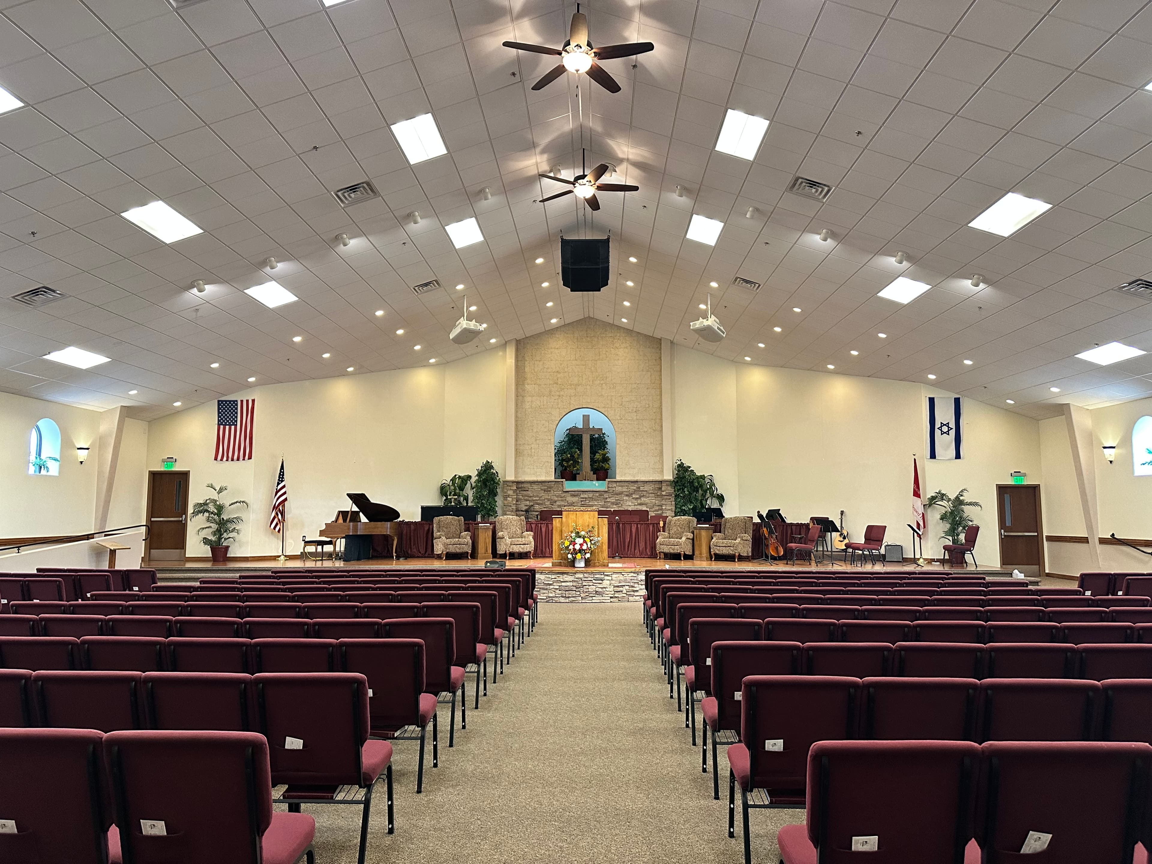 Church sanctuary with maroon chairs, a central pulpit, a cross, and American and Israeli flags.